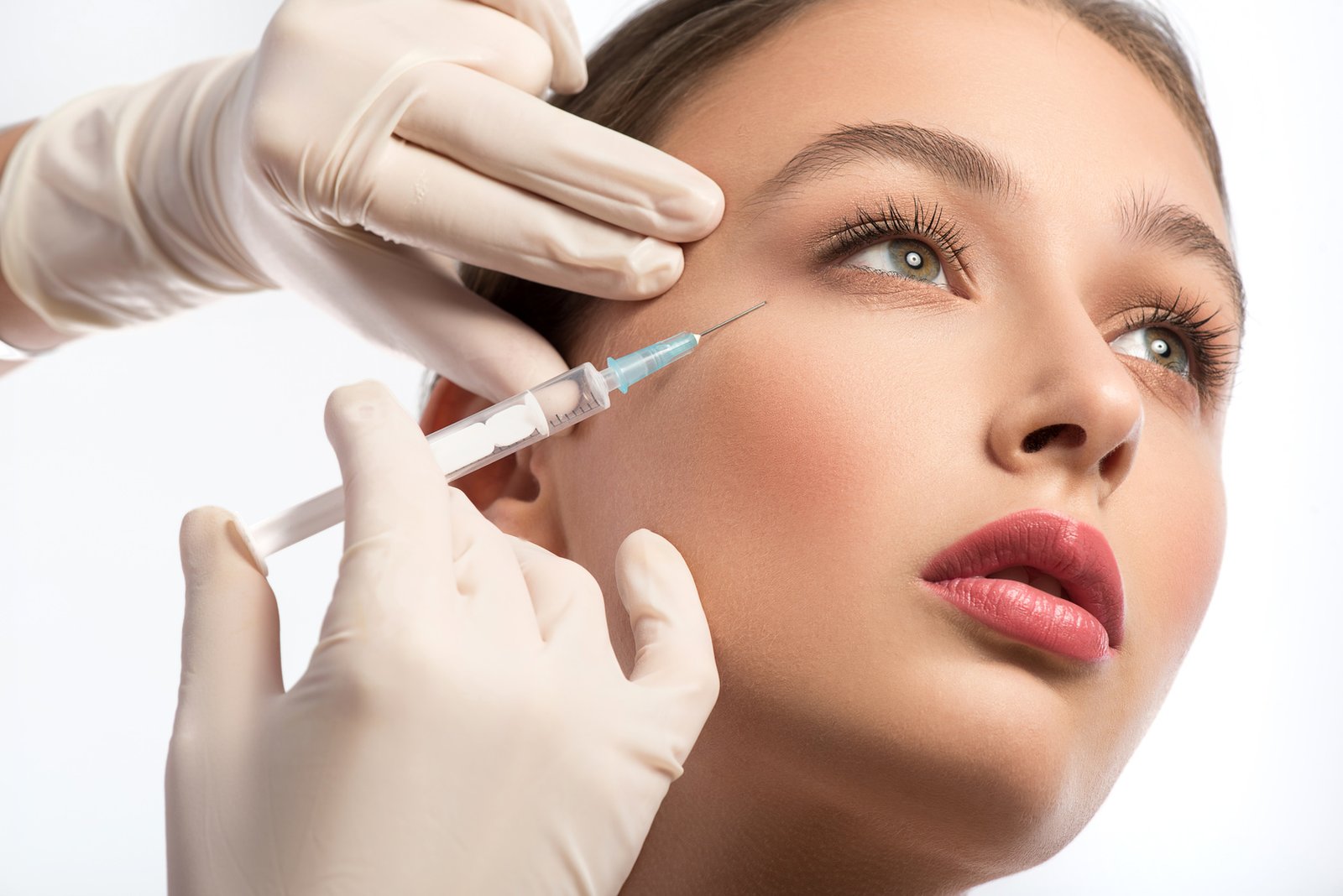Cute girl receiving hyaluronic acid treatment Serine young woman is getting facial botox injection. Beautician hands in gloves holding syringe near her face